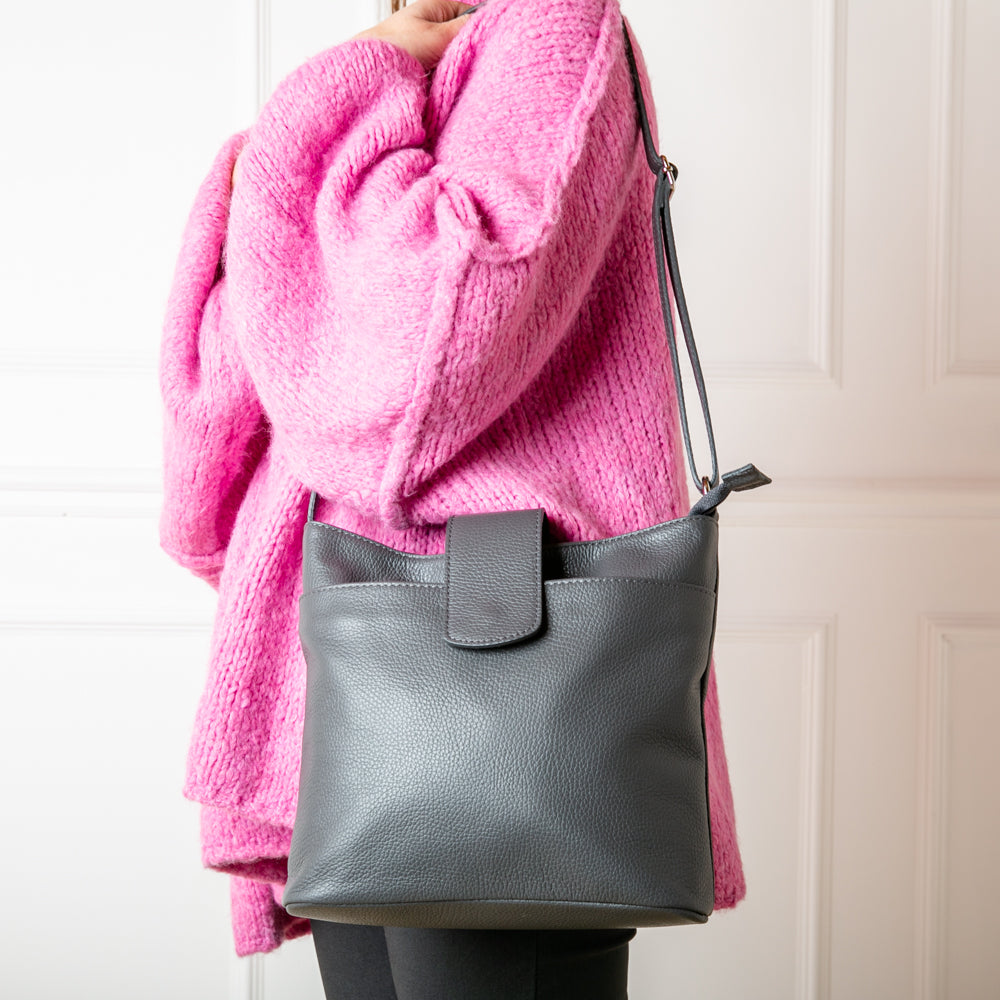 A model wearing the Pimlico Handbag in dark grey, shown from the front and including the adjustable leather strap, the fold over presstud fastening and the outside pocket. Made from Italian leather.